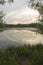 Beautiful nature with pond lake, green trees foliage, grass, observation tower, clouds in the background. Afternoon panorama