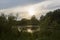 Beautiful nature with pond lake, green trees foliage, grass, observation tower, clouds in the background. Afternoon panorama
