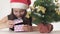 Beautiful naughty girl teenager in a Santa Claus hat secretly looking gift under the New Year tree on white background