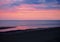 Beautiful near dark twilight over a calm flat sea with purple sky and blue clouds reflected in water on the beach