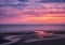 Beautiful near dark twilight over a calm flat sea with purple sky and blue clouds reflected in water on the beach