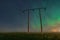 Beautiful night Aurora over double wooden pole power lines in autumn field, front view, starry sky with Aurora Borealis. Sweden,