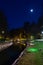 Beautiful night cityscape of a landscaped canal and illuminated walking bridge in the background. Full moon casting light to the s