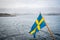 Beautiful nordic archipelago summer view of land and island against sea and hazy horizon with Swedish flag in the foreground.