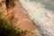 Beautiful ocean shore with golden sand and tidal waves crushing on a beach. Top view of seaside from the green cliff