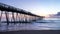 Beautiful ocean sunrise and gentle waves beside an old wooden fishing pier extending far out into the sea.