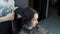 A beautiful Oriental girl sits in a Barber shop while a hairdresser combs her wet hair.