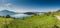 Beautiful panorama lakeside landscape in Switzerland with green fields and blossoming flowers and trees and mountains behind