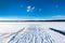 Beautiful panorama winter landscape view of blue sky and frozen snow lake and a jetty with footprints in the snow.