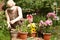 Beautiful pensioner woman florist in face mask take care of pot plants