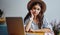 beautiful pensive hipster girl in hat looking at camera working on freelance via netbook
