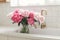 Beautiful peonies in vase in sink on background of brass faucet and white counter in new scandinavian house. Pink peony flowers in