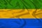 Beautiful photo of the national flag of Gabon on delicate shiny silk with soft draperies, the concept of state power, country life