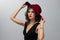 Beautiful photo of a young fashion model with long curly hair in a black long dress and red hat posing on grey background. Concept