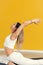 Beautiful pilates or yoga athlete does a graceful pose while wearing a tight sports outfit against a yellow background