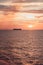 A beautiful pink and gold sunset on the sea, a ship on the horizon, romantic clouds in the sky, a vertical shot