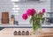 Beautiful pink peonies in a glass vase standing on the kithcen with white brick tile wall.