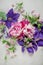 Beautiful pink, rose peonies and violett purple clematis flowers on white wood plate