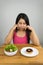 Beautiful plus size Asian woman choosing between salad and chocolate doughnut