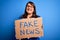 Beautiful plus size woman holding fake news banner for false journalism over isolated background with a happy face standing and