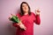 Beautiful plus size woman holding romantic bouquet of natural tulips flowers over pink background Pointing aside worried and