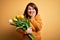 Beautiful plus size woman holding romantic bouquet of natural tulips flowers over yellow background laughing and embarrassed