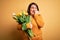 Beautiful plus size woman holding romantic bouquet of natural tulips flowers over yellow background looking stressed and nervous