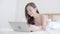 Beautiful portrait asian young woman working online laptop with smile and happy lying on bed