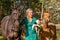 Beautiful portrait of a blond smiling girl with her horse, foal and dog in the forest. Wearing a green dress