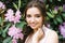 Beautiful portrait of a lovely girl who stands surrounded by lilac pink flowers blooming rhododendron