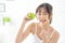 Beautiful portrait young asian woman holding and pointing green apple fruit in the bedroom at home