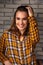 Beautiful positive toothy smiling woman looking happy in casual orange cell shirt on brick blue studio background