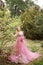 Beautiful pregnant girl in long pink fattini dress touching hand belly and looks at blooming magnolia in park