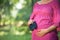 Beautiful pregnant woman with baby shoes stand on green meadow