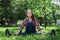 Beautiful pregnant woman in denim overalls sitting on the grass in the park