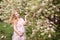 Beautiful pregnant woman in a gently pink dress touches her belly and the other hand touches the flowering tree.