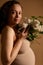 Beautiful pregnant woman, gravid future mother expecting a baby, holding white blooming lilacs, smiles looking at camera