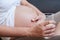 Beautiful pregnant woman holding a glass of milk and keeping a hand on her bare tummy while sitting