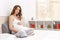 Beautiful pregnant woman holding your big abdomen arms and sitting cross-legged on the sofa indoor.