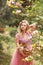 Beautiful pregnant woman in pink dress flowers touches hand belly standing near blooming magnolia tree