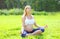 Beautiful pregnant woman sitting on grass doing yoga in summer