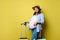 Beautiful pregnant woman smiling looking at camera, posing with suitcases and boarding pass, isolated yellow background