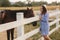 Beautiful pregnant woman stand near the horse. Lady in knitted hat and blue dress. Beautiful farm animal. Brown Hors