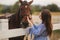 Beautiful pregnant woman stand near the horse. Lady in knitted hat and blue dress. Beautiful farm animal. Brown Hors