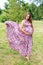 Beautiful pregnant woman walking barefoot in the park in long colorful dress with flying fabric. Happy maternity and fashion