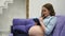 Beautiful pregnant young woman holding a pair of cute baby socks on her bare tummy, lying on her bed at home