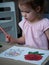 A beautiful preschool girl pensively examines her drawing in a coloring book. Girl paints a flower in her room at a