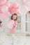 Beautiful preschool girl in a white studio with pink heart-shaped balloons