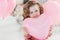 Beautiful preschool girl in a white studio with pink heart-shaped balloons