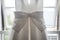 Beautiful pretty big bow on front of brides bright elegant white wedding dress hanging up in the window